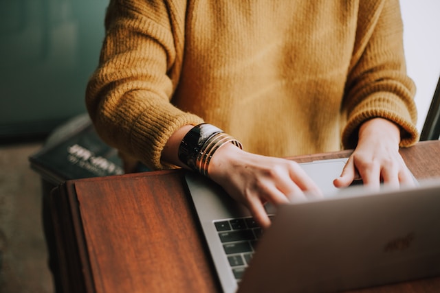 Person with golden sweater and bracelets, types on a laptop keyboard